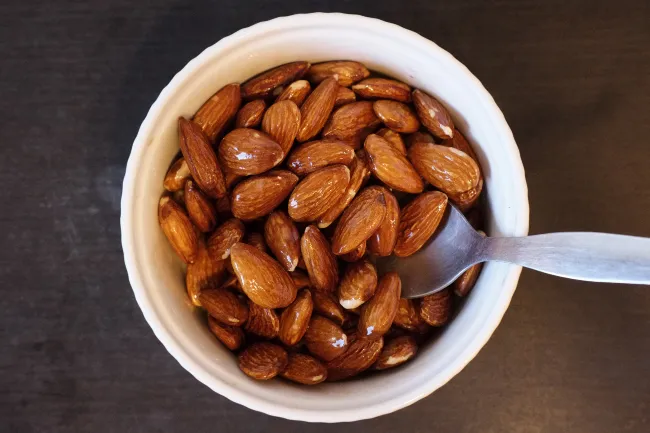 Almonds mixed with olive oil in a white bowl