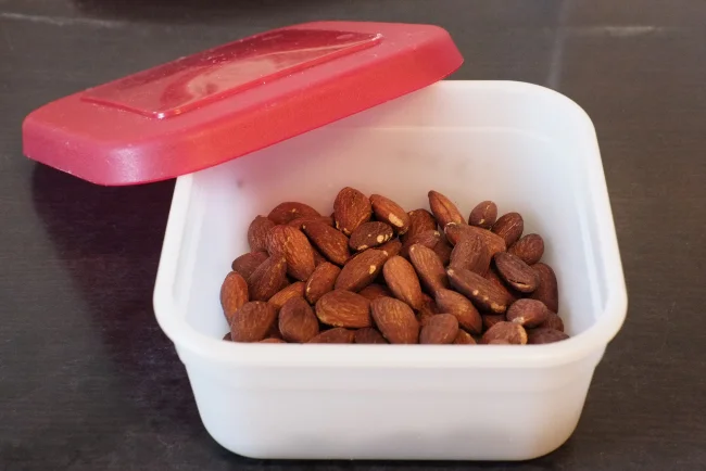 Roasted almonds inside an airtight plastic container about to be stored